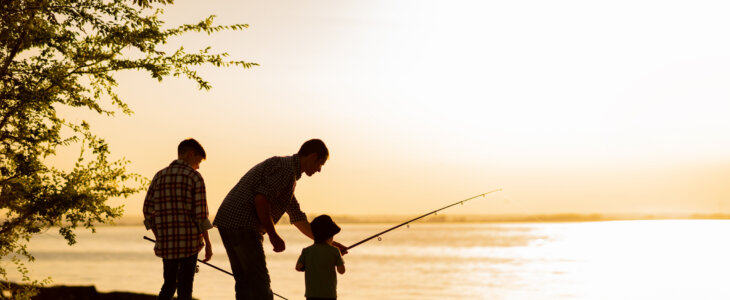 Family dad and two sons are fishing at sunset, silhouette of a man and two boys.
